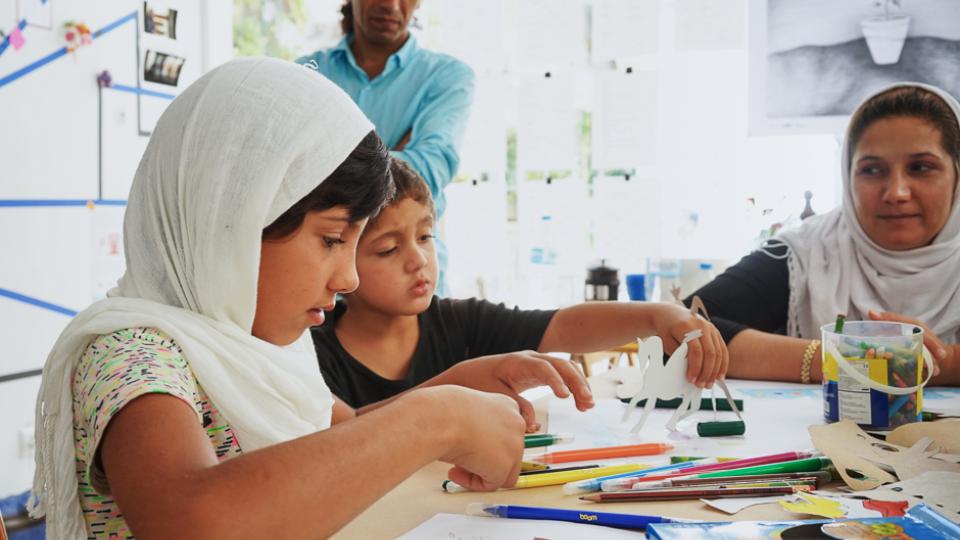 Two children engaging in artwork with paper cutouts, markers and pens.