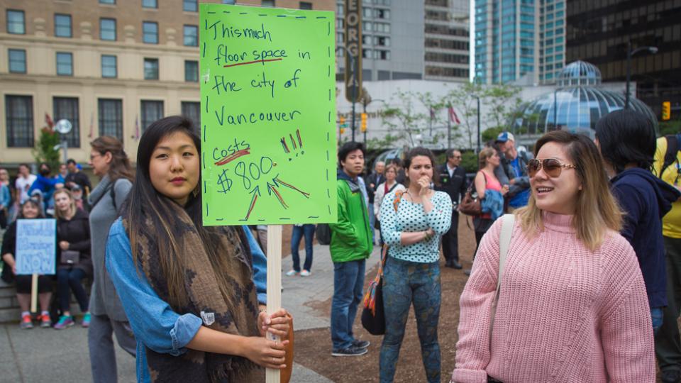 A girl holding a placard that reads, "This much floor space (size of placard) in the City of Vancouver costs $800!!!" at an Affordable Housing Protest Rally in Vancouver, Canada.