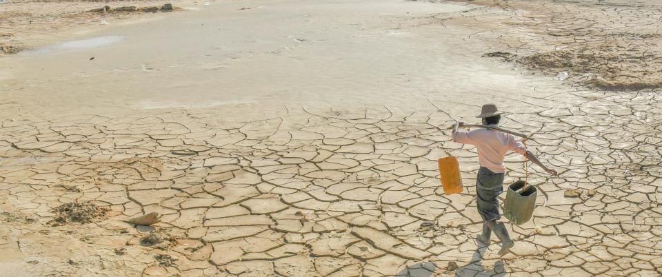 Man carrying water on cracked dry land in Sagaing Region, Myanmar