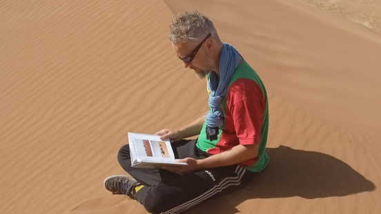 UNU-EHS expert Kees van der Geest looking at a book in the desert