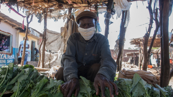 A farmer, wearing a mask, under a shack with his produce