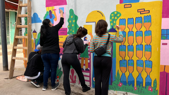 Three women are painting a colourful mural. 