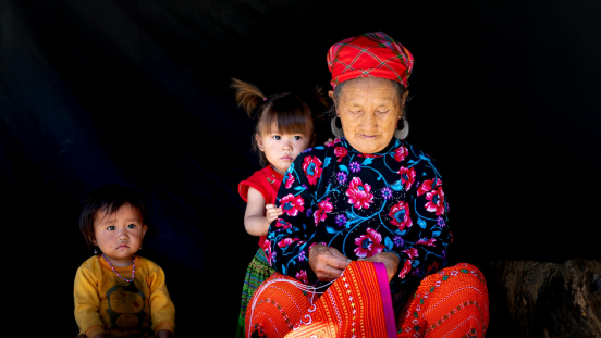 An elderly woman with two small kids on her lap and by her side.