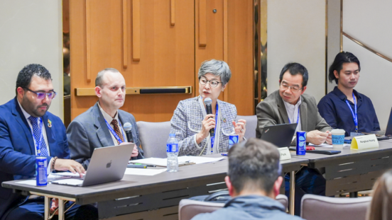 Panel of speakers on a conference session, with the session moderator speaking on the microphone.