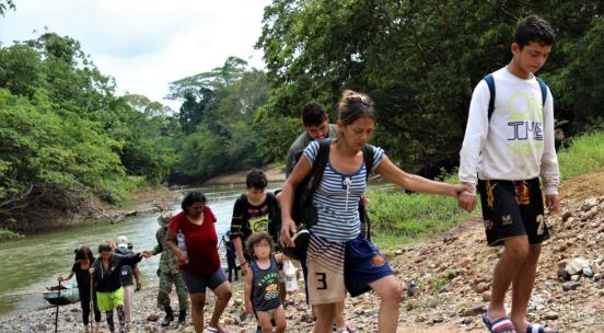 Group of migrants, including young children, cross a rocky hill