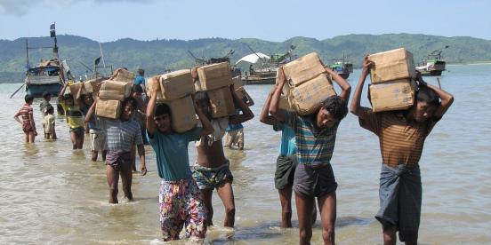 Rohingya refugees wading through water carrying supplies on their heads