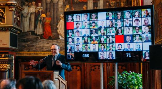 UNU-CRIS event with Philippe De Lombaerde standing at a podium with a screen behind him displaying profile pictures of UNU-CRIS personnel