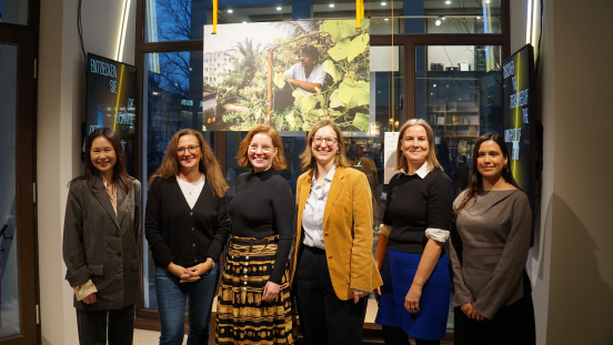 Six people pose in front of a photo at an exhibition.