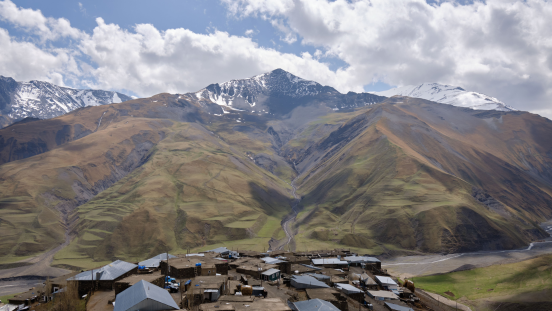 On the forefront there is a little village, with mountains in the background.