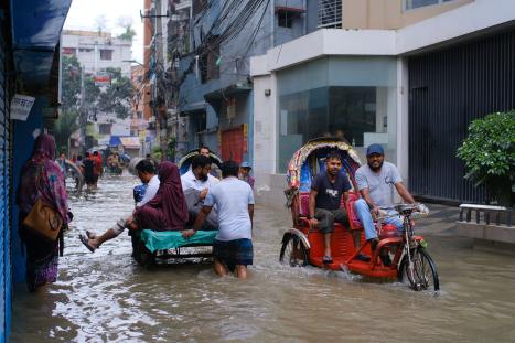 People and rickshaws navigate a flooded urban street after heavy rain.
