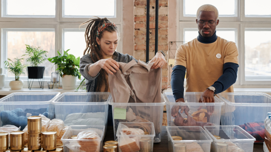 A woman and a man organize donated clothes and food in see-through boxes.