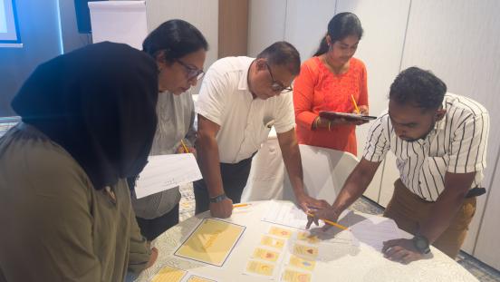 Participants collaborate around a table during a workshop activity, reviewing cards and worksheets while taking notes.