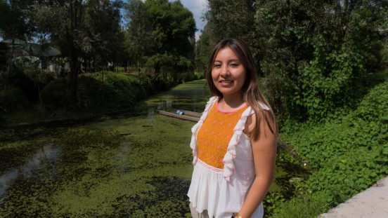 A woman stands in front of a canal covered in duckweed.