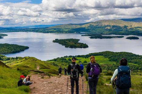 LOCH LOMOND, UNITED KINGDOM - MAY 31 2022: Hikers and walkers descending Conic Hill overlooking Balmaha and Loch Lomond in the Scottish Highlands.