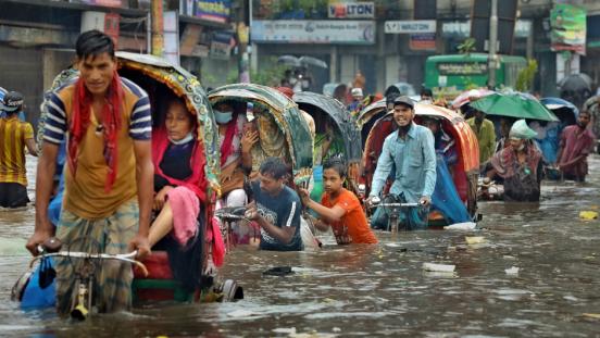 People in cycle rickshaws trying to drive through a flooded street in Dhaka.