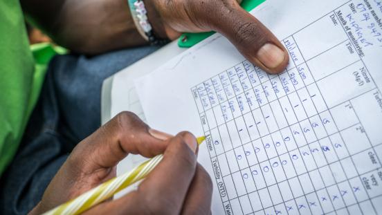 The hands of a citizen scientists recording Nitrate and turbidity data on a sheet of paper with a pencil.