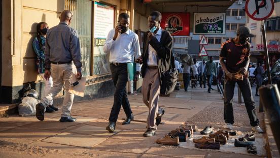 Two men wearing masks walking down a busy street in Kampala, Uganda.