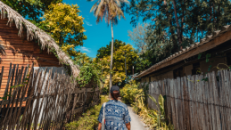 Woman walks on a small road in between two houses on a tropical island