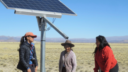 Three women talk under a solar panel
