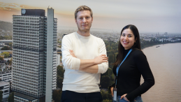 Two people standing in front of a background of a UN building at the river Rhine. 