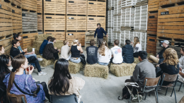 A learning session with a group of people, young and old, in a makeshift venue (barn/warehouse).