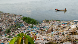 A man in a wooden boat amid a load of plastic trash in the water