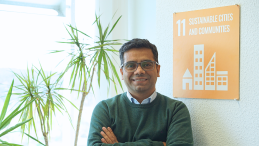 A male scientist stands in his office in front of a poster of SDG 11