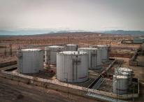 Aerial view of large industrial oil tanks in a desert setting with mountains in the distance