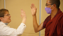 A woman with short hair high fives an Asian monk in a burgundy robe.