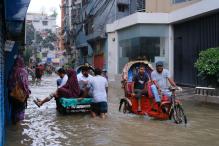 People and rickshaws navigate a flooded urban street after heavy rain.