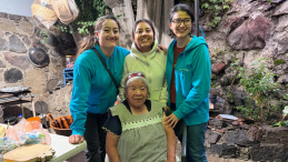 Four women pose for a picture. Three younger woman stand behind an elderly woman in a chair. 