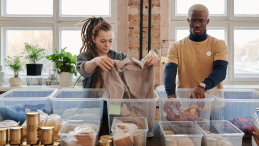 A woman and a man organize donated clothes and food in see-through boxes.