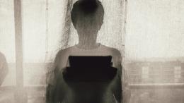 A silhouette of a person using a tablet device behind a curtain indoors