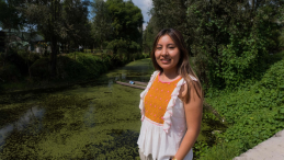 A woman stands in front of a canal covered in duckweed.