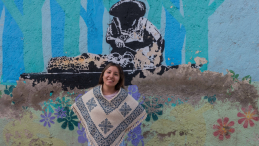 A women stands in front of a murral in Mexico City. 