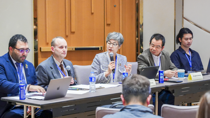 Panel of speakers on a conference session, with the session moderator speaking on the microphone.