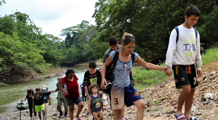 Group of migrants, including young children, cross a rocky hill