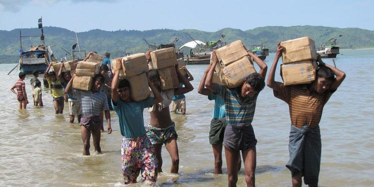 Rohingya refugees wading through water carrying supplies on their heads