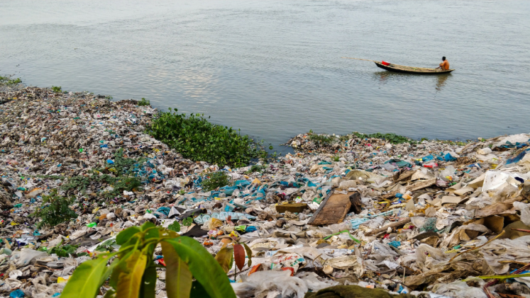 A man in a wooden boat amid a load of plastic trash in the water