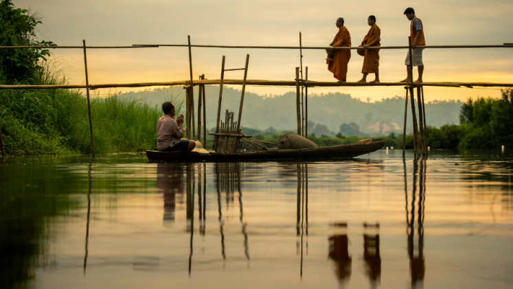 A fisherman in a wooden boat watches three men cross a bridge