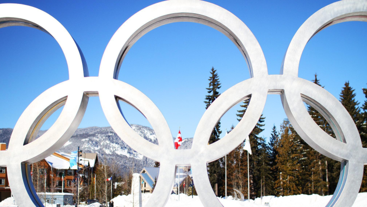 The Olympic rings in front of a snowy, mountainous background. 