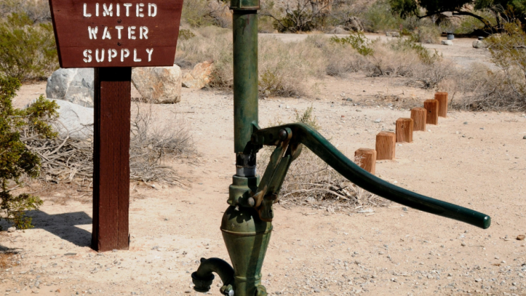 A groundwater pump in front of a sign that says limited water is available.