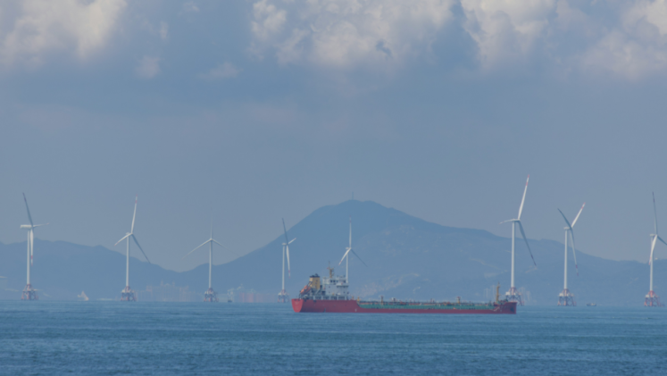 A tanker sails in front offshore wind turbines. 