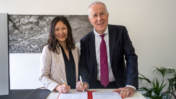 A woman and a man smile for the camera after signing a document.
