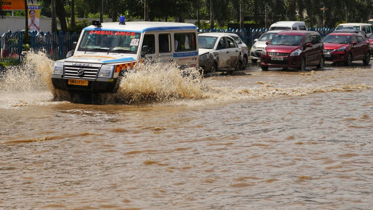 An ambulance drives through a flooded street, followed by other cars.