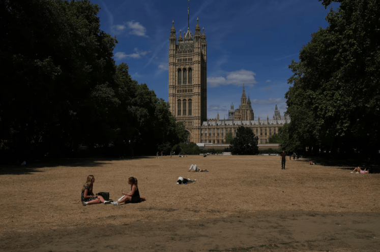 People sit on dried grass in a park outside the Houses of Parliament in London, Monday, Aug. 10, 2026. (AP Photo/Kin Cheung)