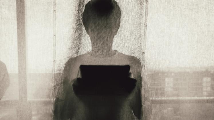 A silhouette of a person using a tablet device behind a curtain indoors