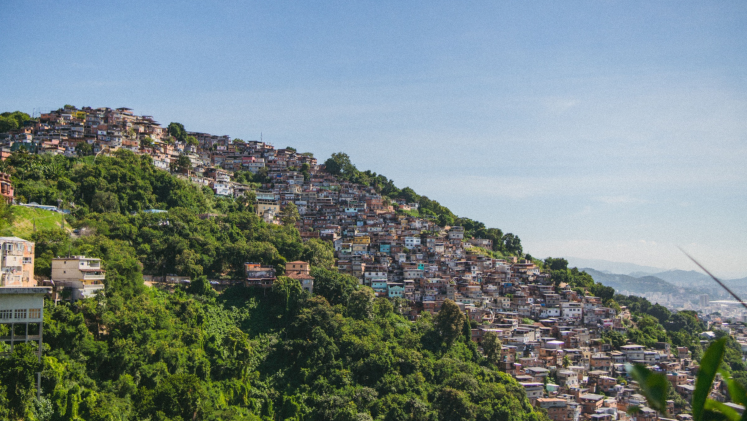 A colourful favela against a green hillside.