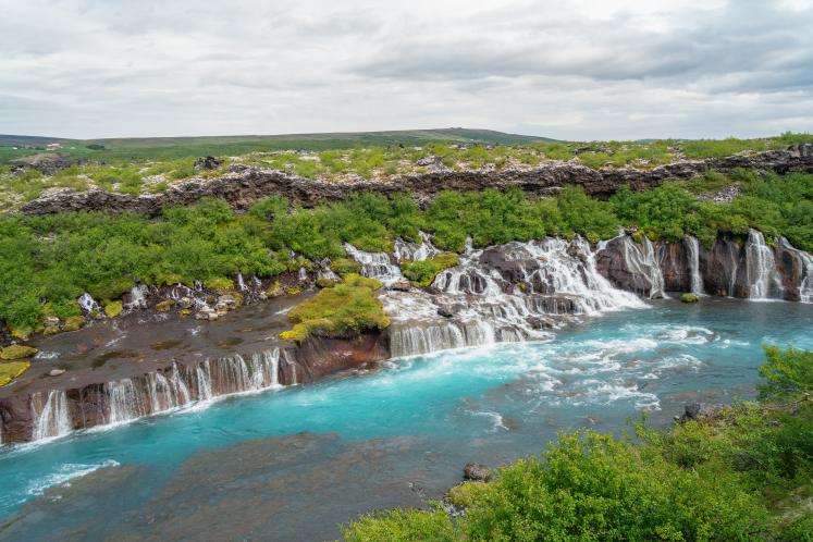  Waterfall flowing from beneath a lava field into the bright turquoise water of the Hvita river in Iceland. September 26, 2026