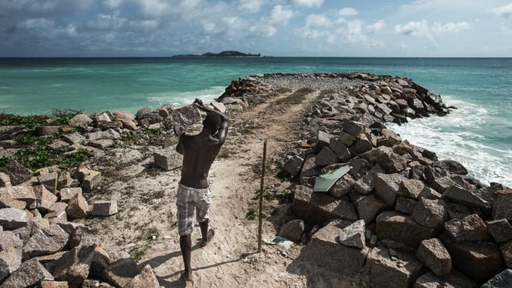 A man carrying a large rock to use in protecting the coast at Anse Kerlan beach in Seychelles.